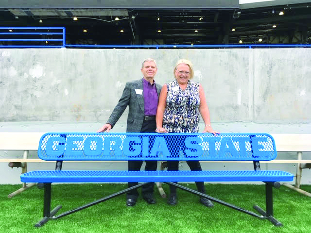 2 white people stand next to a bench at the Georgia State Stadium